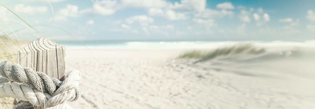 Ein großer menschenleerer Sandstrand, rechts kann man noch ein paar Dünen sehen, weiter im Hintergrund sieht man das Meer